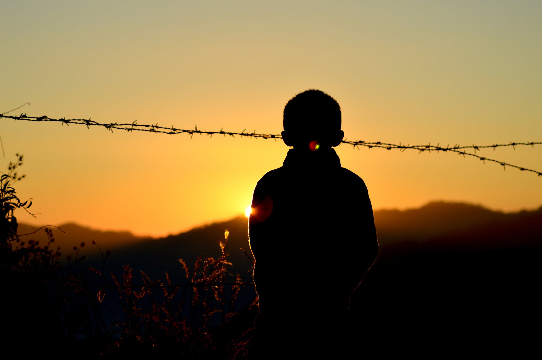 silhouette of boy standing near barbed wire fence during golden hour